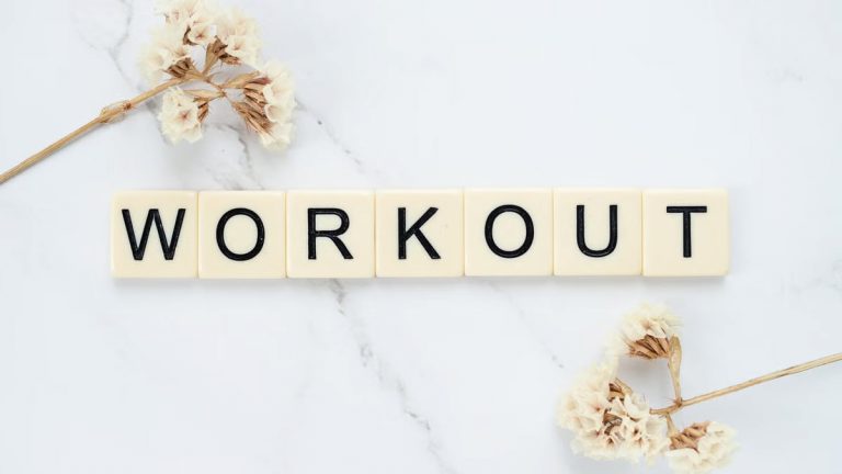 Letter tiles spelling 'WORKOUT' on marble with dried flowers, conveying fitness motivation.