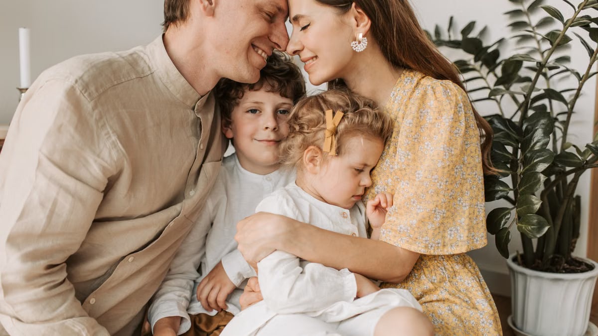 A loving family of four shares a tender moment in a cozy indoor setting, embracing and smiling.